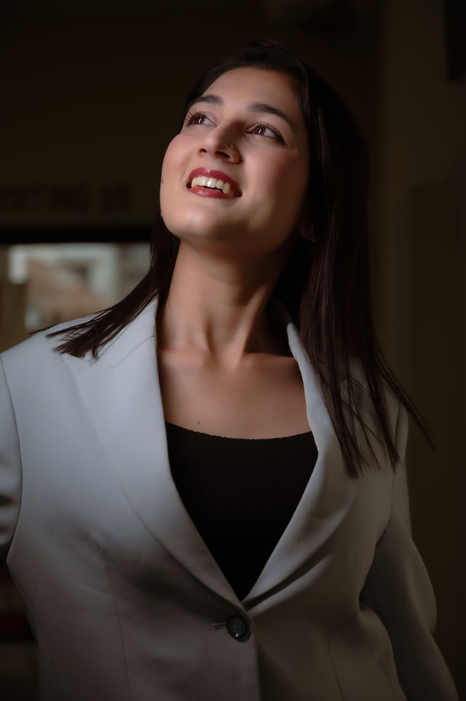 Professional woman in a blazer smiling brightly indoors, exuding confidence and elegance.